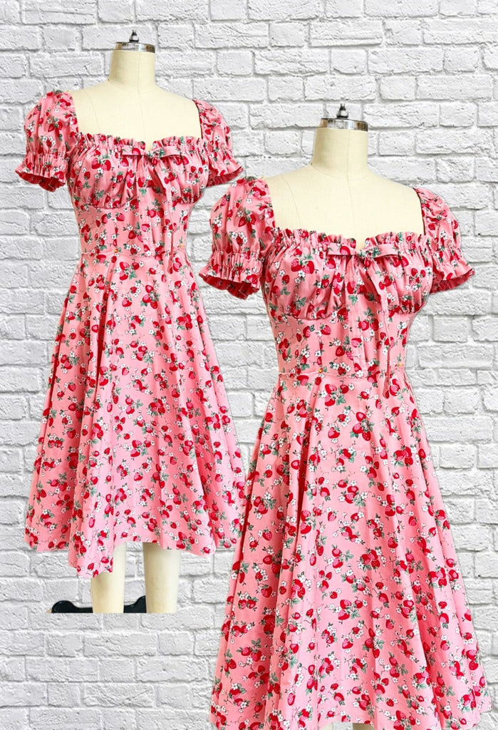 Mannequin form showing the Abigail dress in pink strawberry print cotton features puff sleeves, a corset style bodice with gathered cups, tie up front, circle skirt with side seam pockets, and is fully lined.