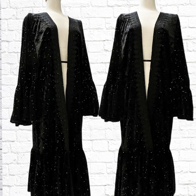 Mannequin forms showing the Our Angelica Robe has an open centre front trimmed in heavy gimp lace, large ruffled hem, and Angel Wing sleeves in a beautiful Twilight Glitter Velvet in front of a white brick backdrop.