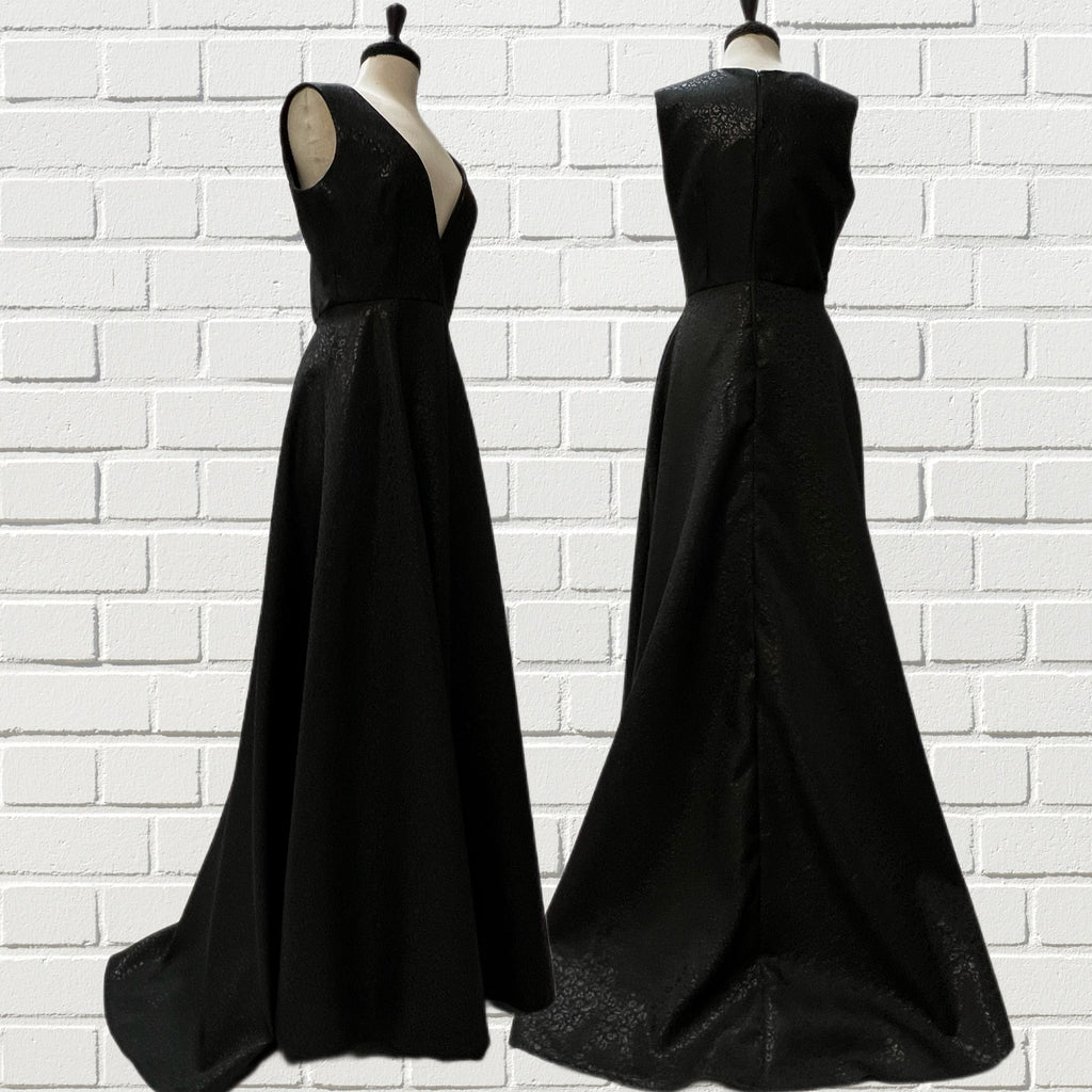 Mannequin forms in front of white brick showing the Ava Gown with its black-on-black floral brocade gown with a V-neckline, fitted bodice, side seam pockets, and slight train.