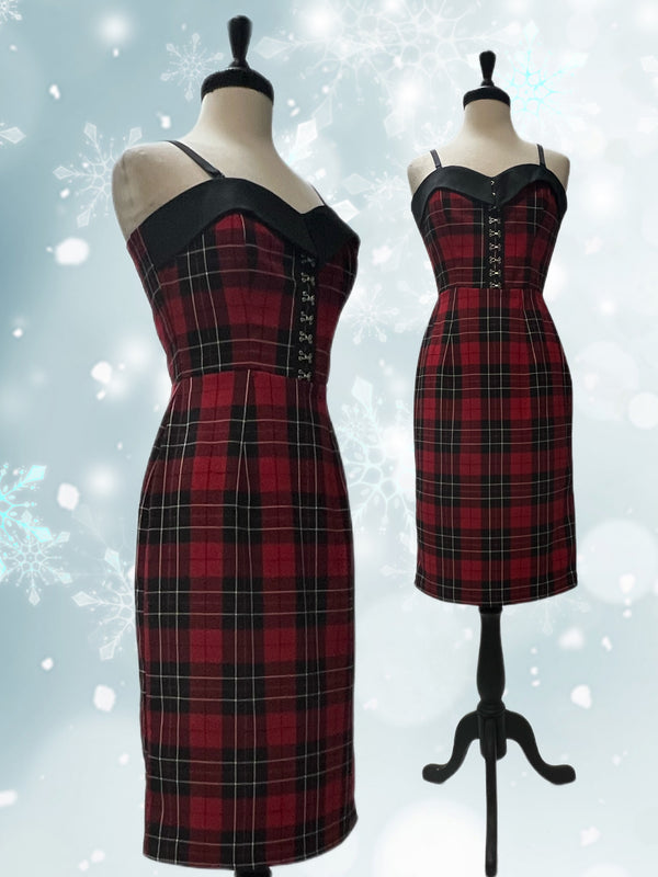 Mannequin forms showing the Bettie Pencil Dress in plaid with fitted bodice, contrast black bodice flap, detachable spaghetti straps, black and metal hook & eye centre front detail, and back skirt vent against a snowflake backdrop.