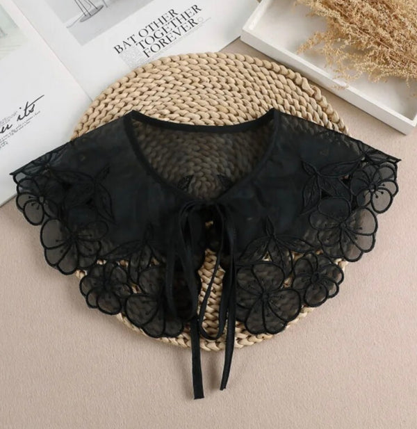 A detachable black lace collar is displayed against a woven coaster on a white table.