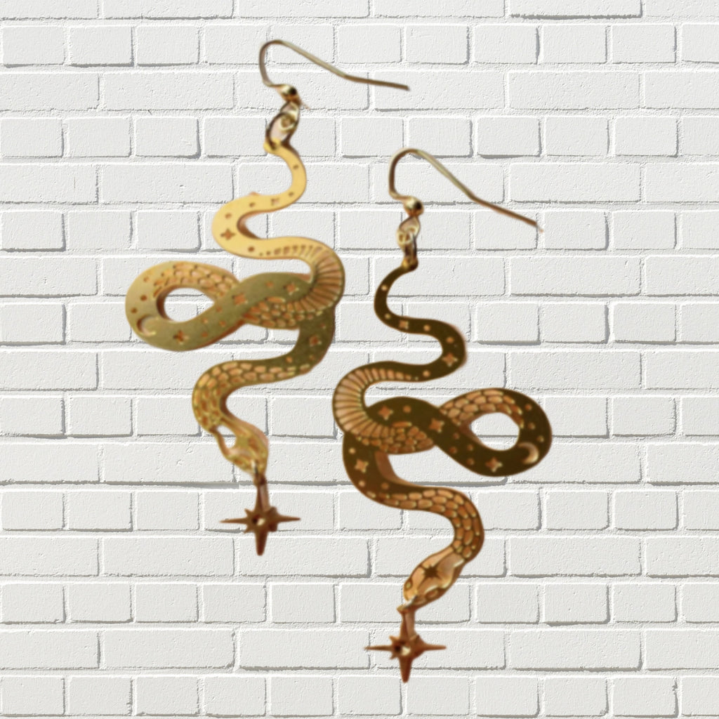 Delicate cutout snake earrings in vibrant gold against a white brick background.