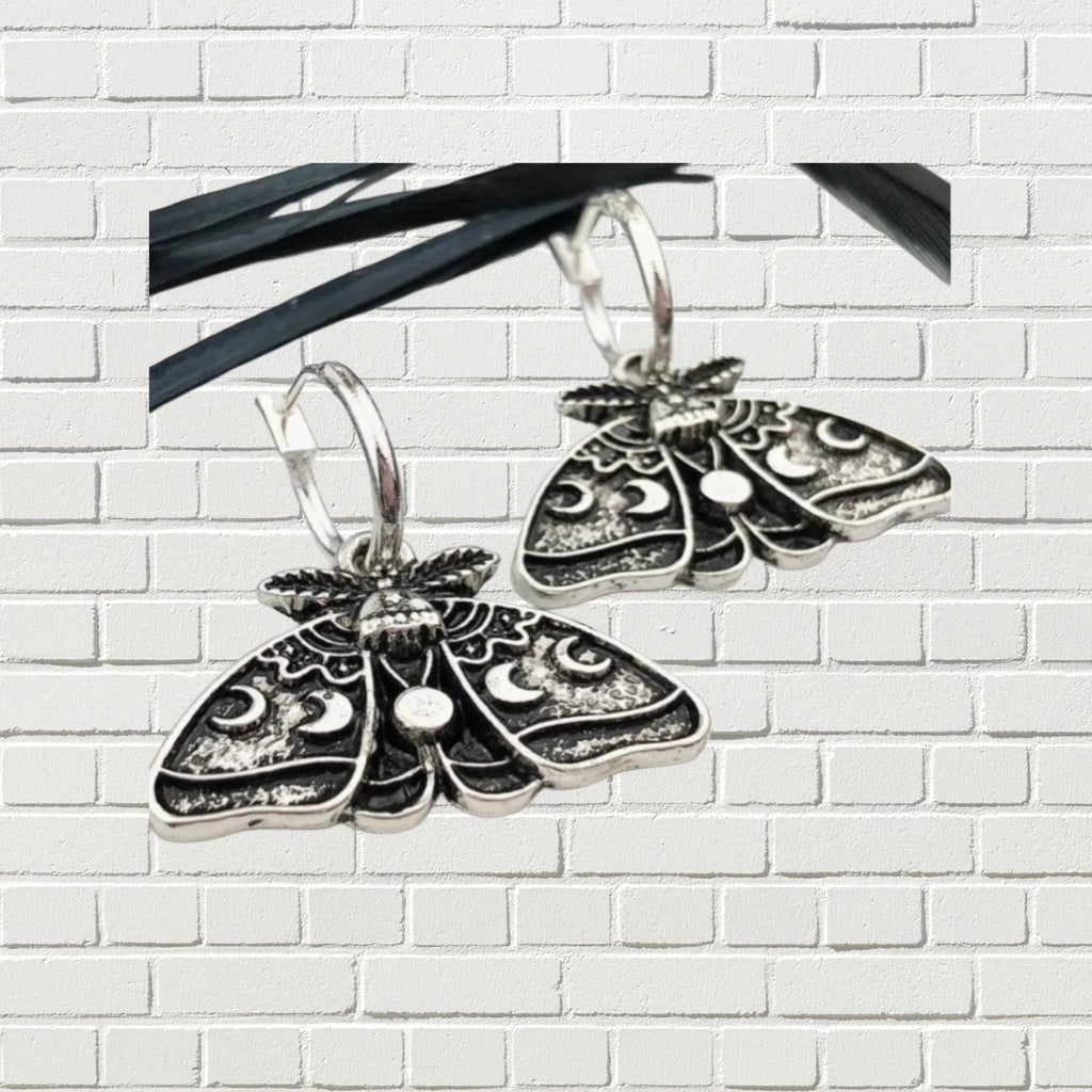 Silver moth hoop earrings against a white brick backdrop.