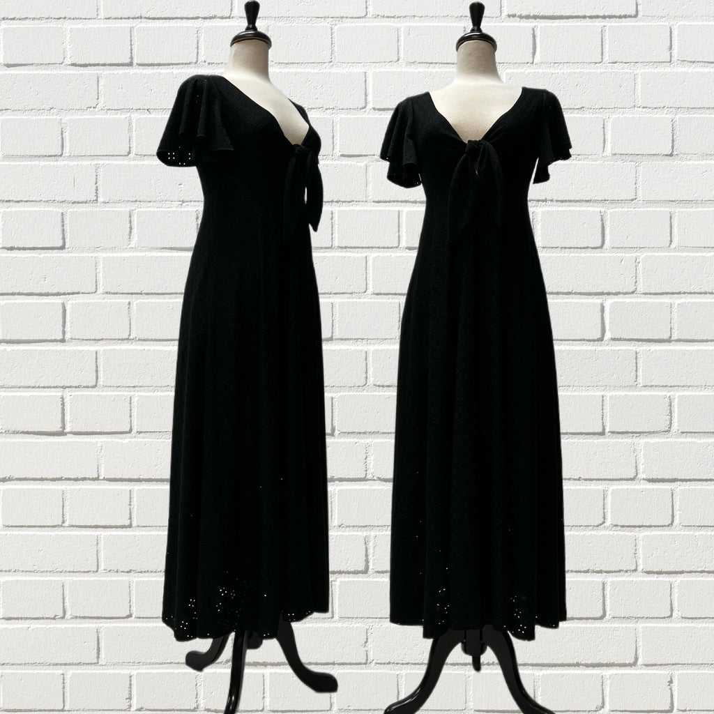 Mannequin form showing a Cotton blend Erin dress in black eyelet with a tie up front, flutter sleeves, raise empire waist and A-Line, and 1/2 lined skirt. 