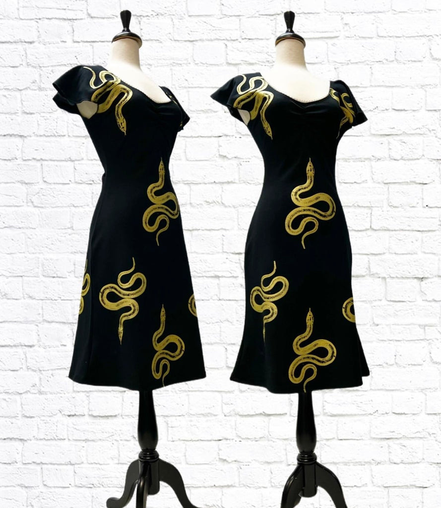 Mannequin form showing Our gold-on-black double knit Ponte  “Caution, Snakes” print Maggie dress with flutter sleeves and slight tulip hem in front of a white brick backdrop.