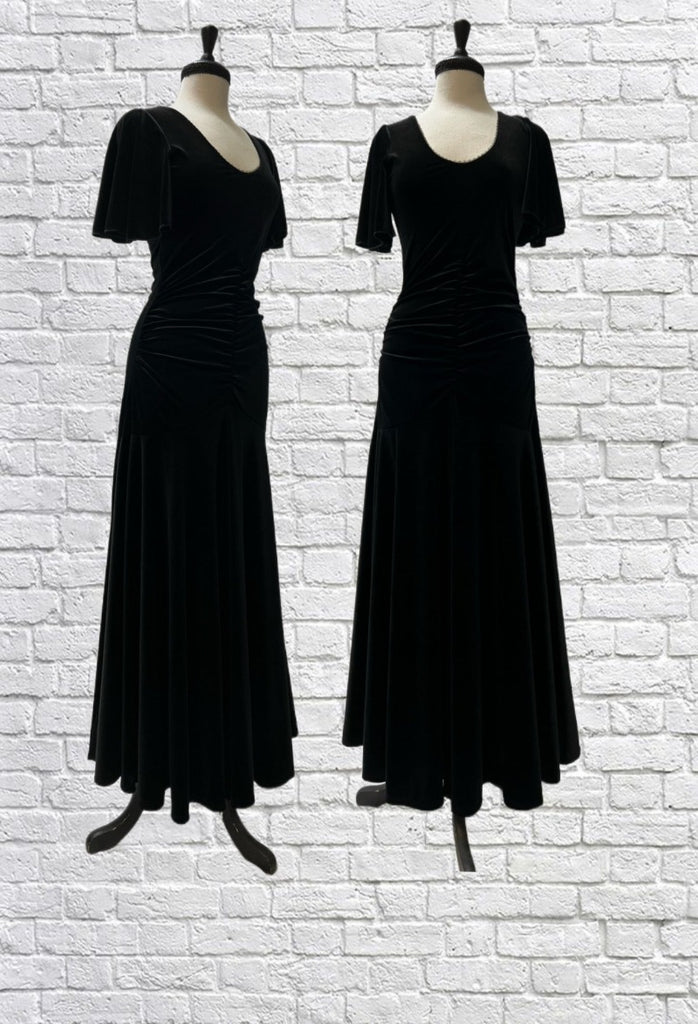 Mannequin forms in front a white brick background showing the Ophelia Gown in beautiful stretch black velvet with scoop neck, flutter sleeves, and ruching down the centre front and back. 