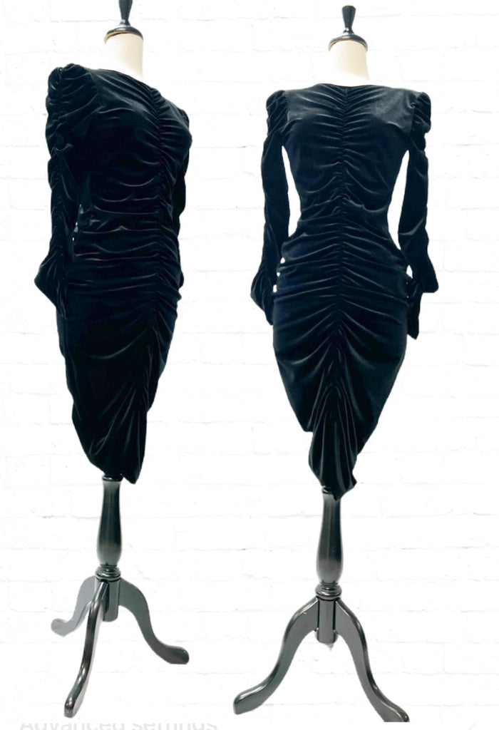 Mannequin forms in front of a white brick background showing the Ruby Pencil Dress in Black Velvet with Ruching down the front and back with even more ruching down the sleeves.