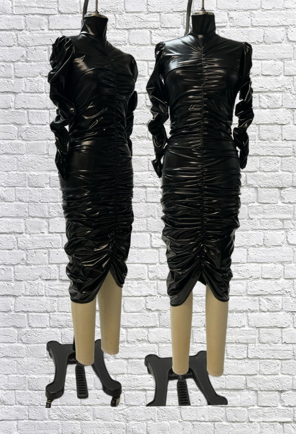 Mannequin forms in front a white brick background showing the Ruby Ruched Pencil Dress, which is a Ruby dress in black stretch PVC with ruching on the sleeves, and centre front and back. 