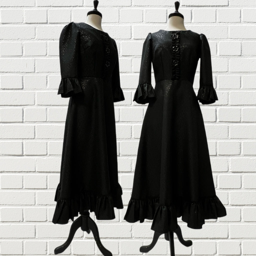 Mannequin forms in front of a white brick background showing the Valerie Dress featuring a ruffle front, 3/4 length ruffle sleeves, an A-line skirt with side seam pockets, micro pleat ruffle hem, and full lining. 