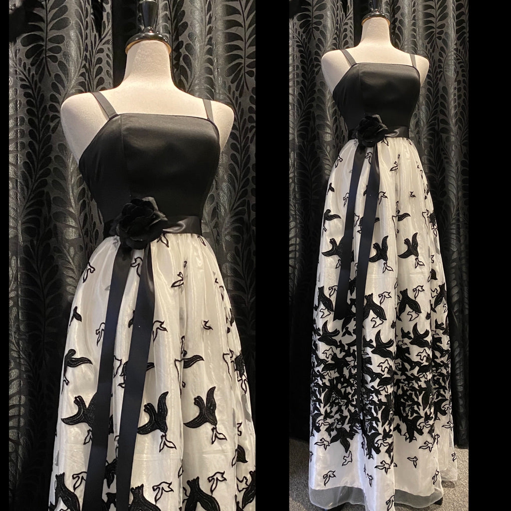Mannequin forms showing off the Brigit Gown in Black Peau du Soie and Sequin Mesh, with a fitted bodice, sleeveless, detachable bra straps, gathered Maxi Skirt in white with sequin embellished Blackbirds. 