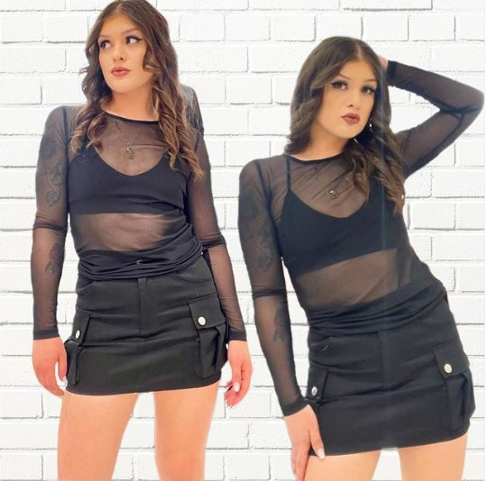 A brunette model wearing a black cargo skirt with a black mesh top over a black lace bralette.