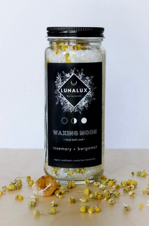 Glass jar of bath soaks in the scent rosemary and bergamot showing here with a piece of citrine resting against it.