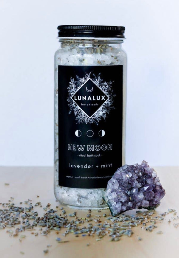 Glass jar of bath soaks in the scent lavender and mint, shown here with a piece of amethyst. 