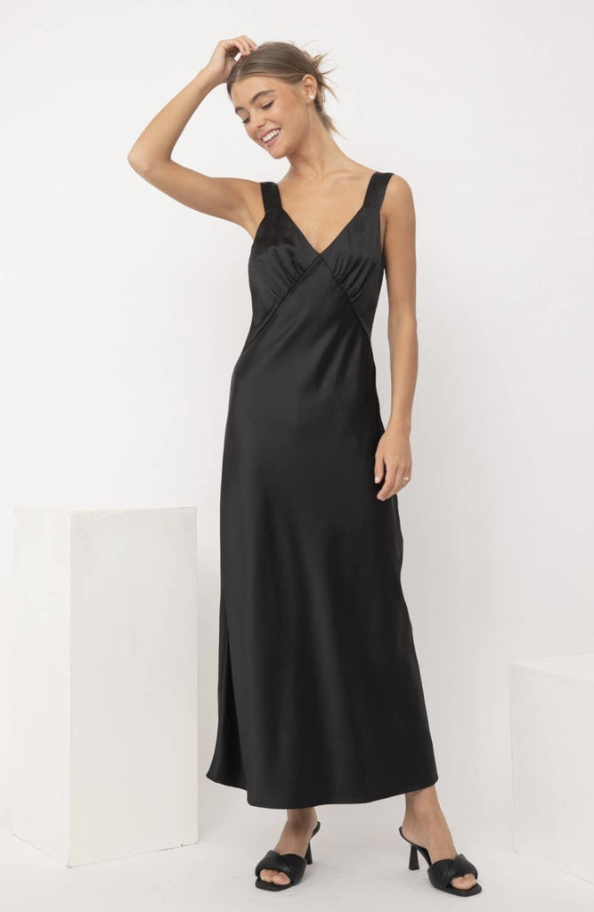 A model showing the front view of a black silk slip dress.